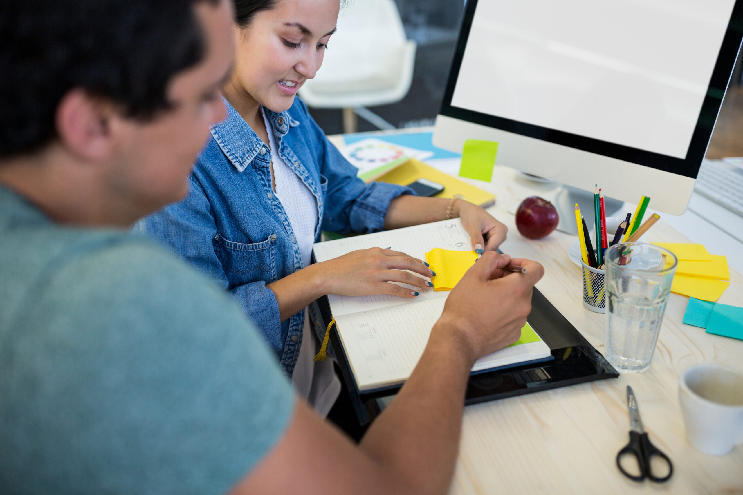 Male and female graphic designers writing on diary